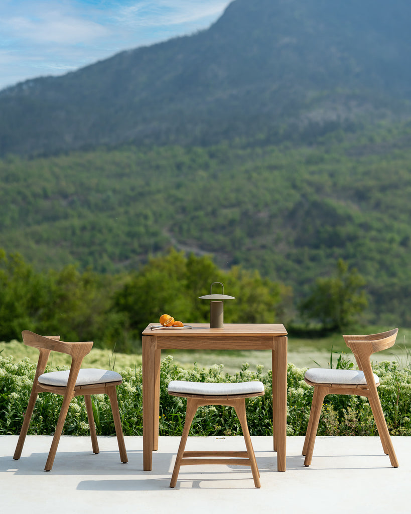 Outdoor furniture set with table and chairs in a scenic setting with mountains and greenery.