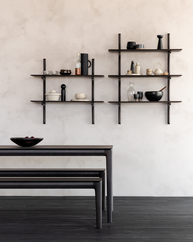 Dining area with a table and wall-mounted shelves against a plain wall.