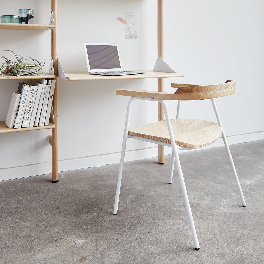 Minimalist desk setup with a laptop, books, and a chair in a room.