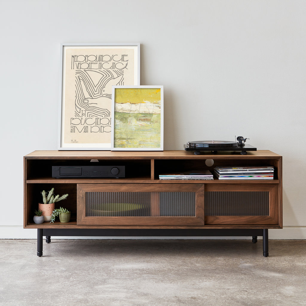 Wooden entertainment console with shelves and a turntable, featuring two framed artworks on a light gray wall.
