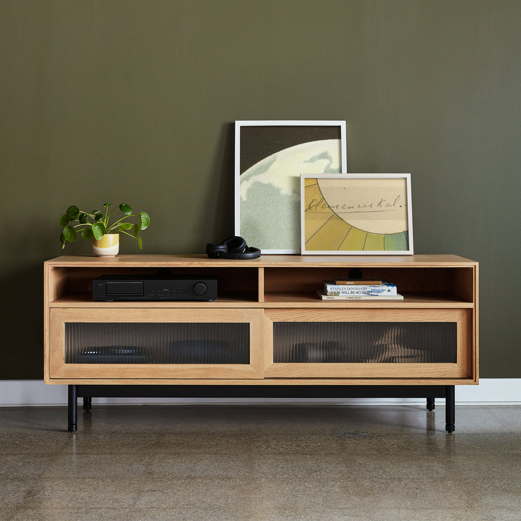 Wooden entertainment console with framed pictures and a plant against a green wall.