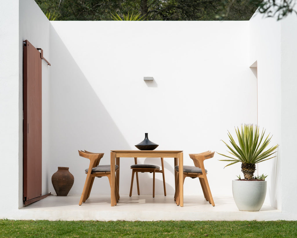 Outdoor patio with wooden table and chairs, potted plant, and white walls.