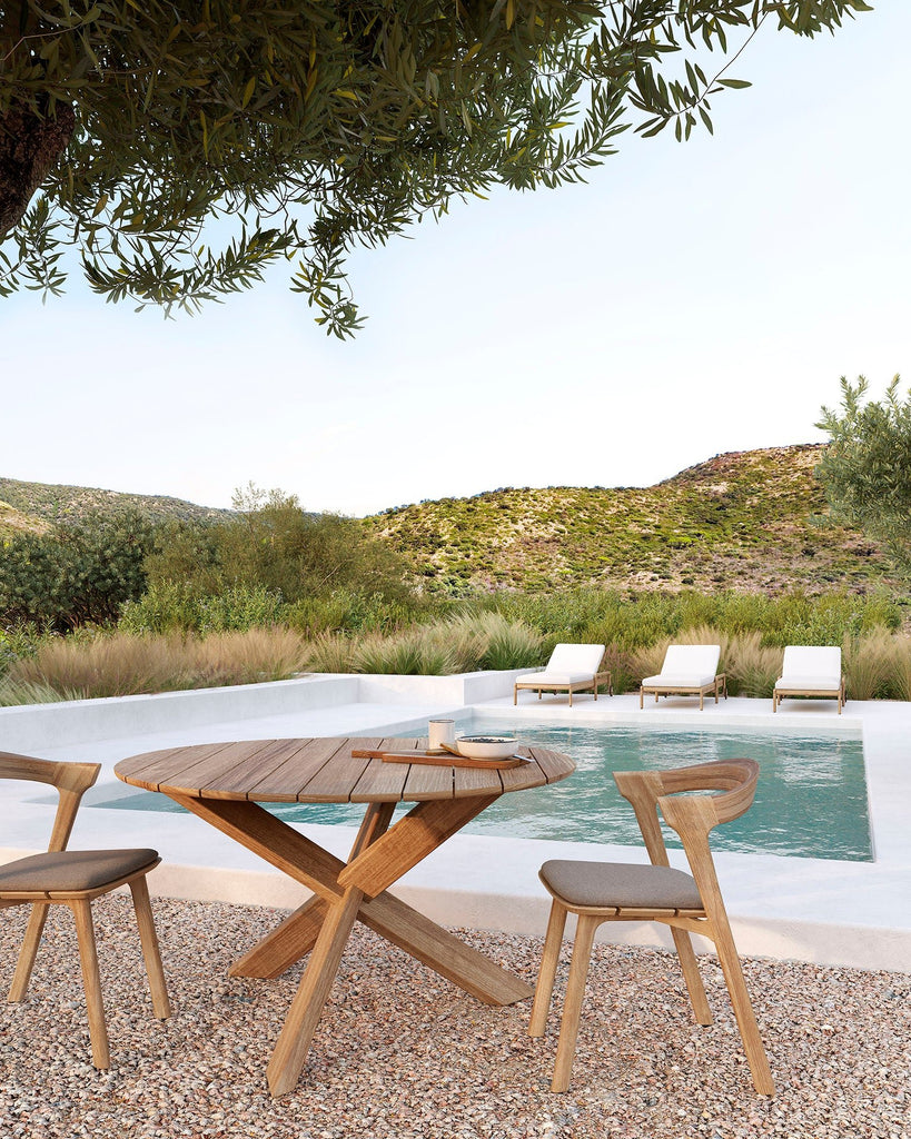 Outdoor setting with wooden table and chairs near a pool with a scenic background