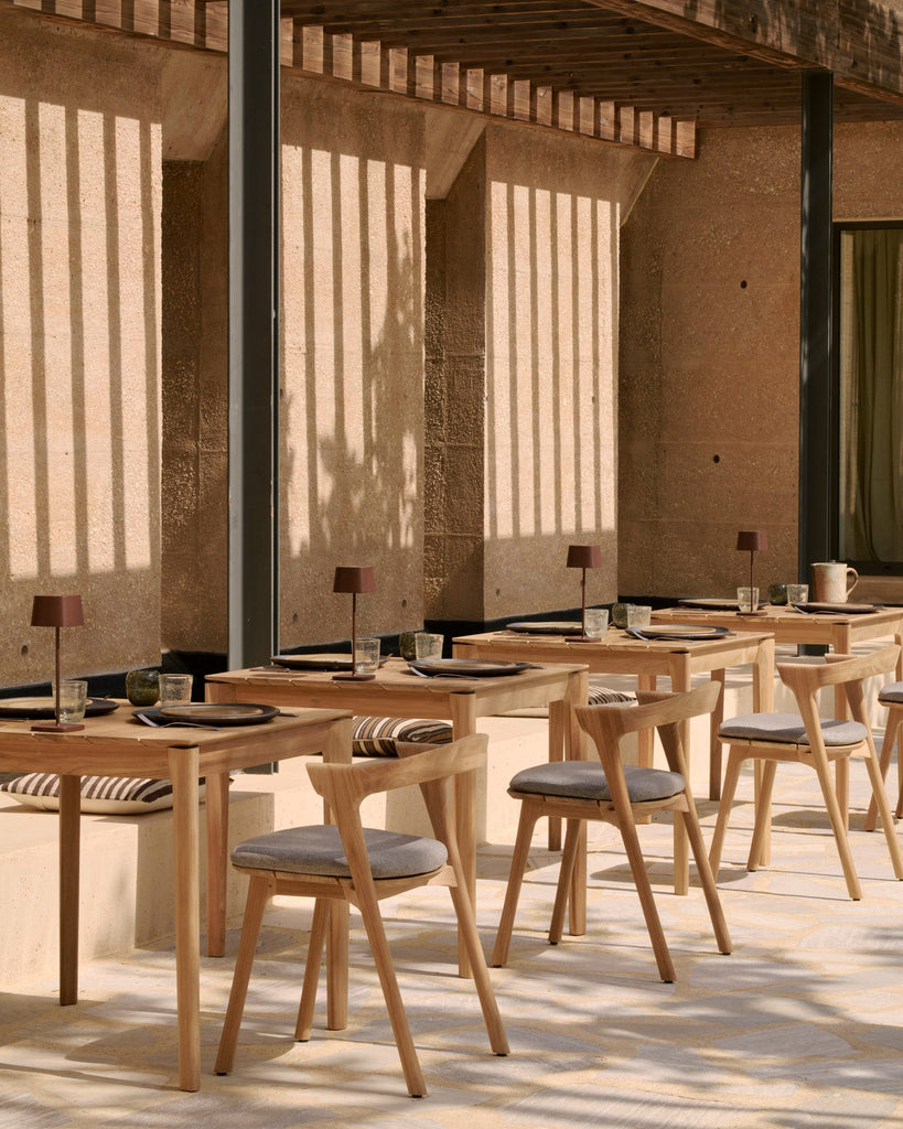 Outdoor dining area with wooden tables and chairs in a sunlit setting.