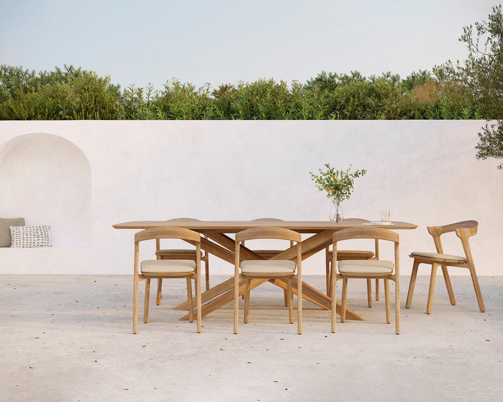 Wooden dining set with table and chairs on a patio with greenery in the background