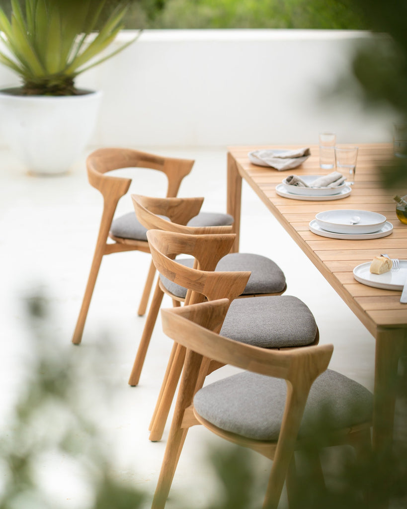 Wooden dining table with chairs and plates on a blurred outdoor background