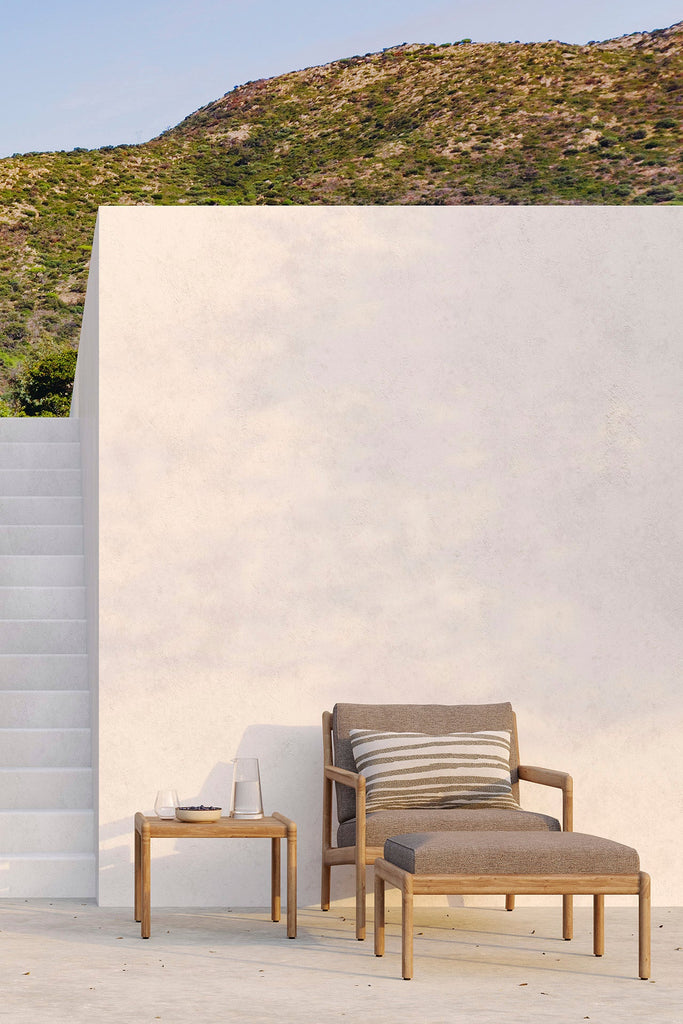 Outdoor lounge chair with ottoman and small table against a white wall with mountainous background