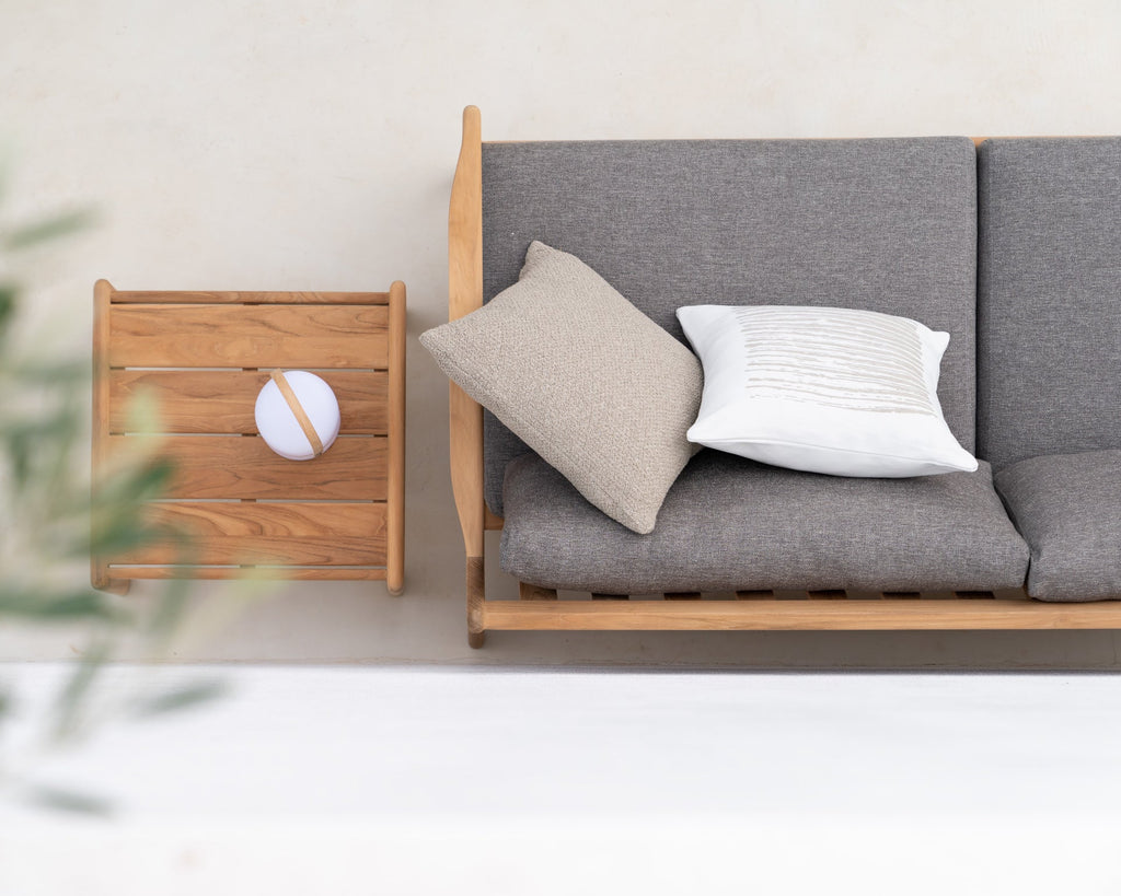 Gray sofa with wooden frame and two cushions next to a wooden side table with a spherical object on a light gray background.
