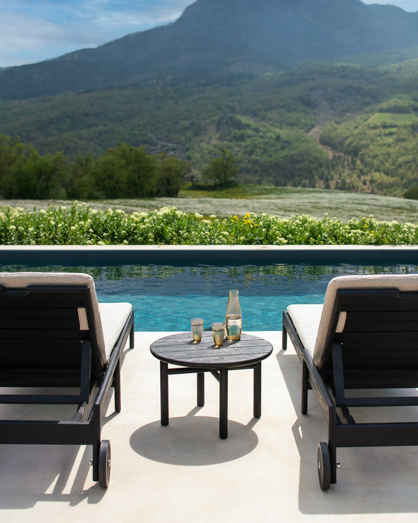 Outdoor patio with lounge chairs and a table by a pool with mountains in the background