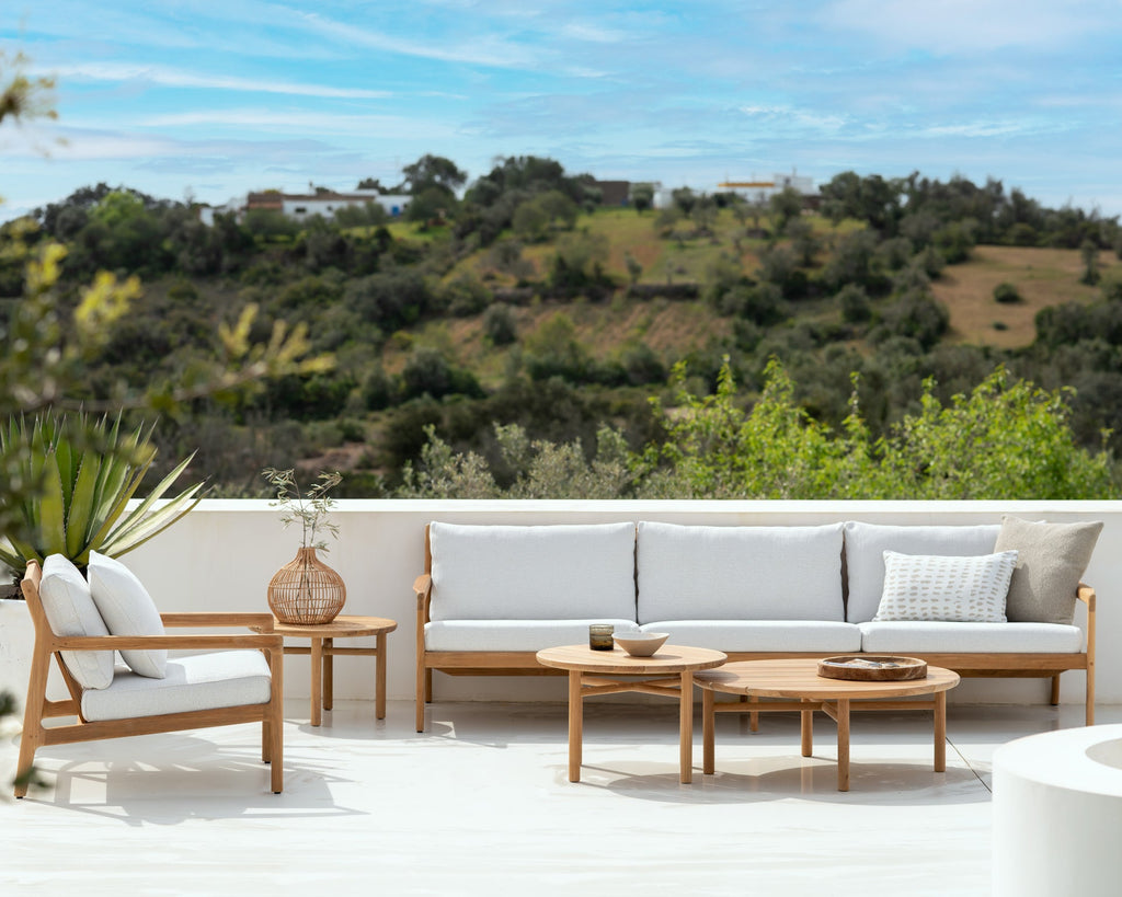 Outdoor patio set with wooden furniture and white cushions on a balcony with a scenic view.